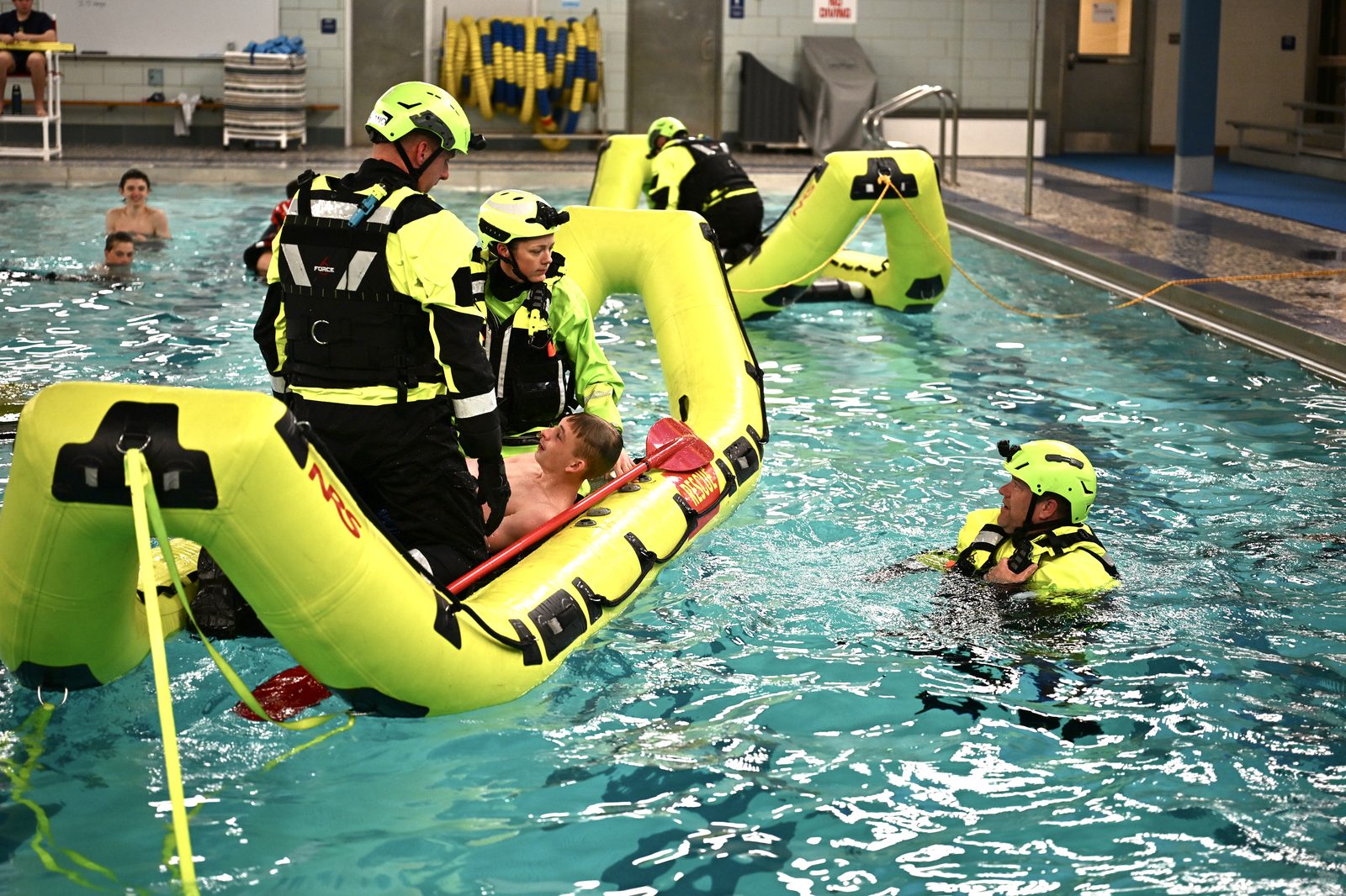 Rescue swimmers in NRS gear kneeling on inflatable raft during water rescue drill