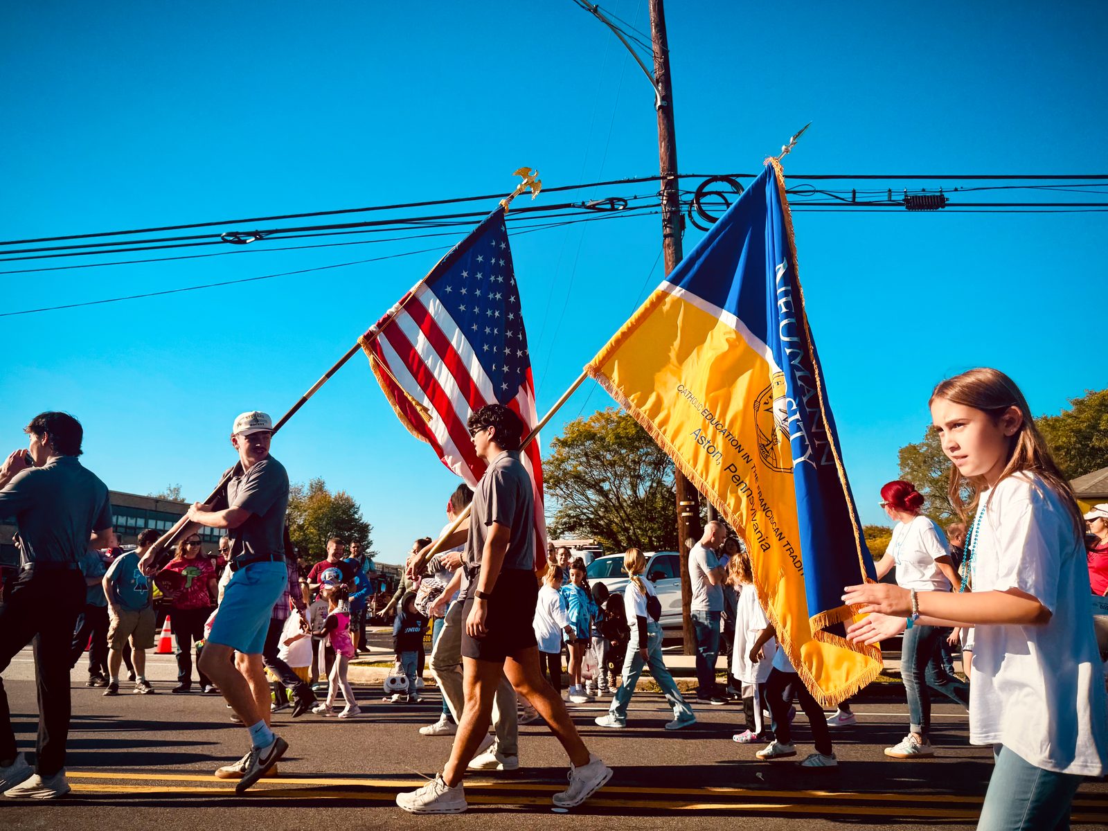 Community members marching with American flag and Neumann University banner at Aston Township parade