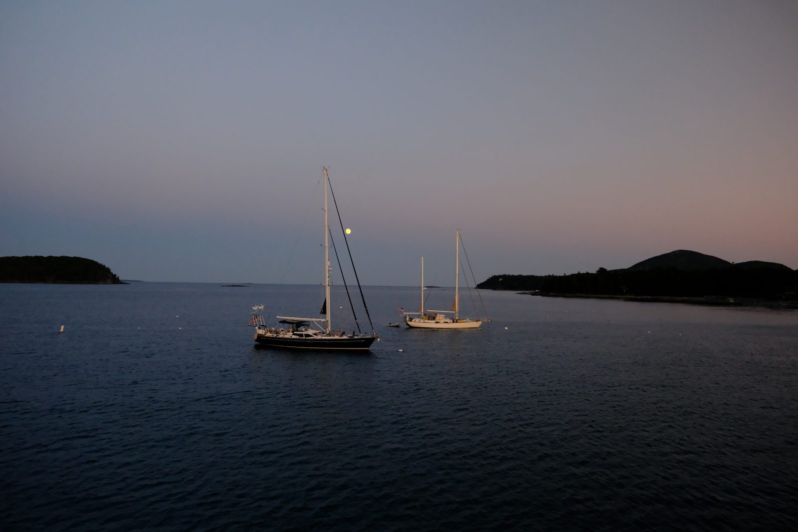 Sailboats anchored at twilight with moonrise off the Maine coast
